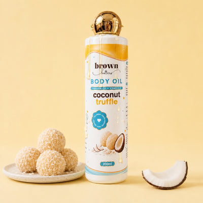 Brown Butters Coconut Truffle Body Oil bottle on a warm yellow background with coconut flakes and a coconut slice