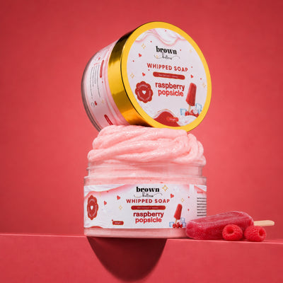 Brown Butters Raspberry Popsicle Whipped Soap in a clear jar with lid propped above and raspberries on pink