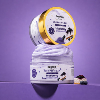 Brown Butters Blueberry Cheesecake Whipped Soap swirled in a clear jar with its lid and a dessert prop on purple