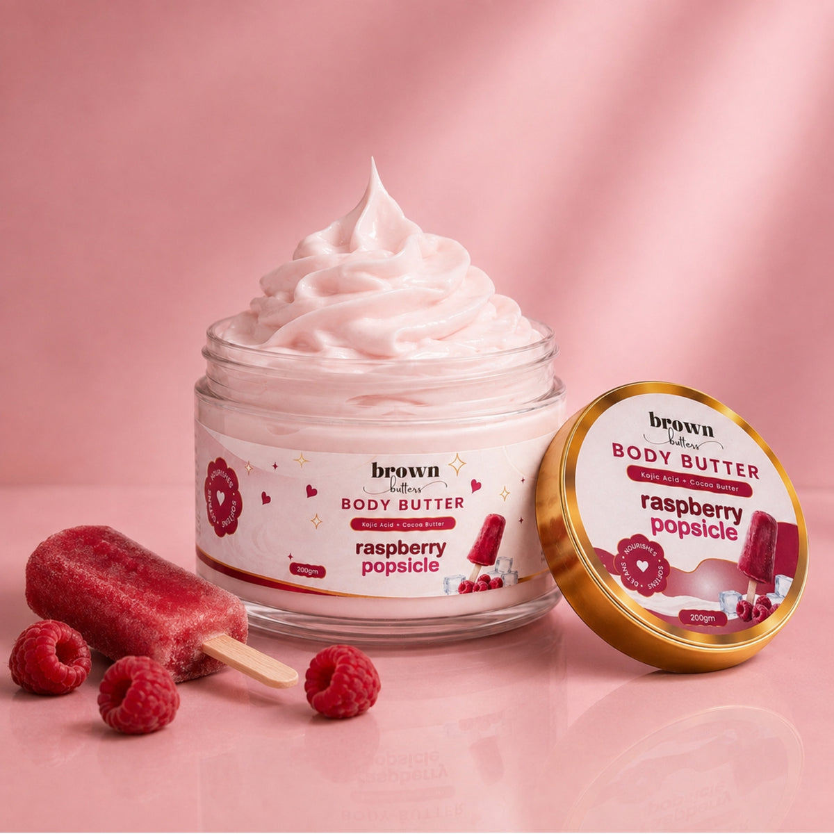 Brown Butters Raspberry Popsicle Body Butter jar of pink whipped cream with gold lid, popsicle and raspberries