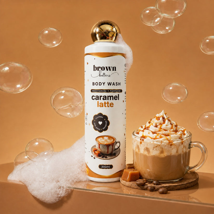 Brown Butters Caramel Latte Body Wash bottle beside a whipped latte with cream, bubbles and foam on tan