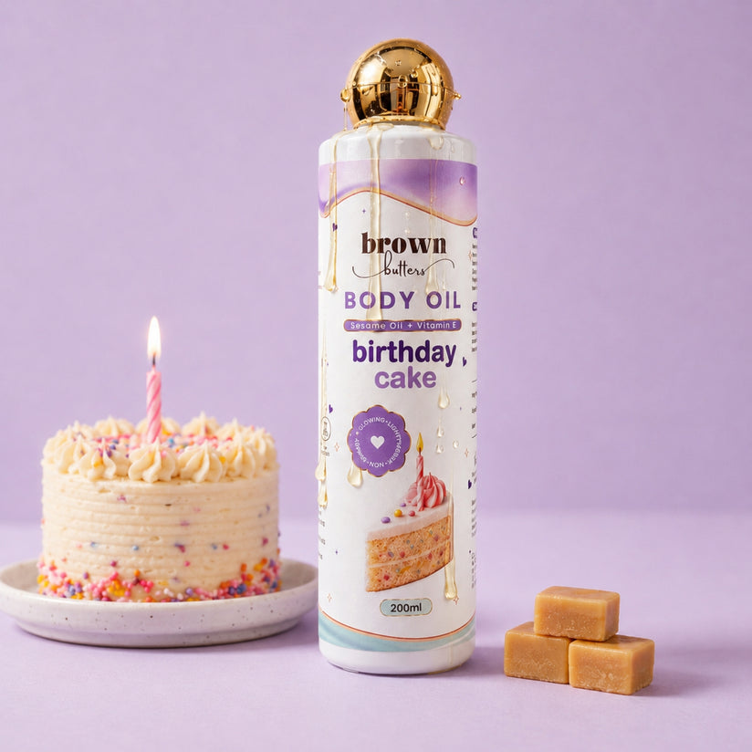 Brown Butters Birthday Cake Body Oil bottle with gold cap on lavender, styled with a small cake and caramel cubes
