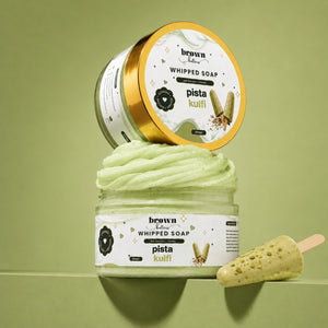 Brown Butters Pista Kulfi Whipped Soap in a clear jar with gold lid and a soap popsicle prop on light green