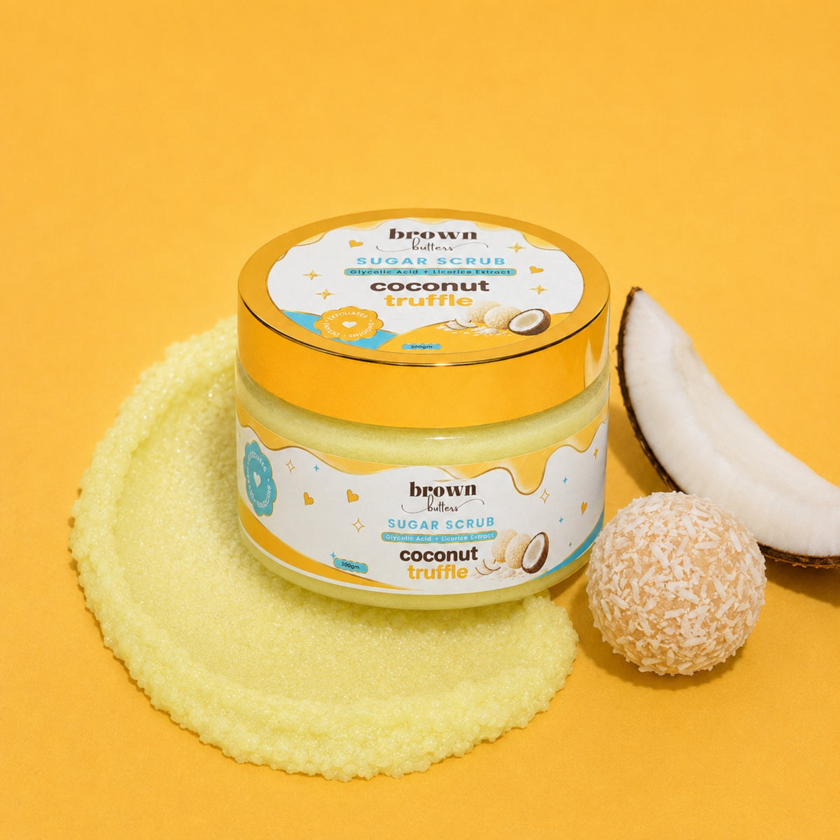 Brown Butters Coconut Truffle Body Scrub jar on yellow with a scrub smear, coconut half and coconut-coated truffle