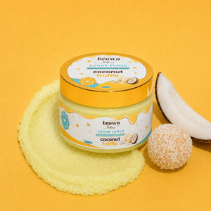 Brown Butters Coconut Truffle Body Scrub jar on yellow with a scrub smear, coconut half and coconut-coated truffle