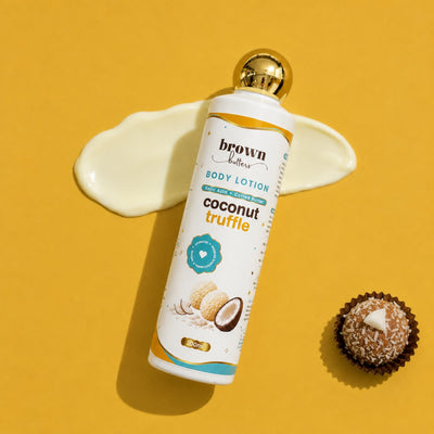 Brown Butters Coconut Truffle Body Lotion bottle with gold cap on yellow, with a cream smear and a truffle cookie
