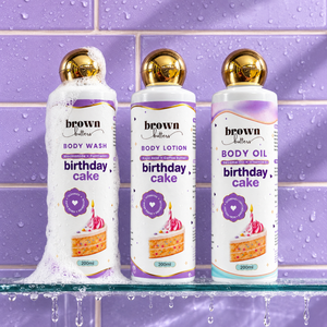 Brown Butters Birthday Cake Body Wash, Lotion and Oil bottles on a wet purple tiled shelf