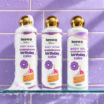 Brown Butters Birthday Cake Body Wash, Lotion and Oil bottles on a wet purple tiled shelf