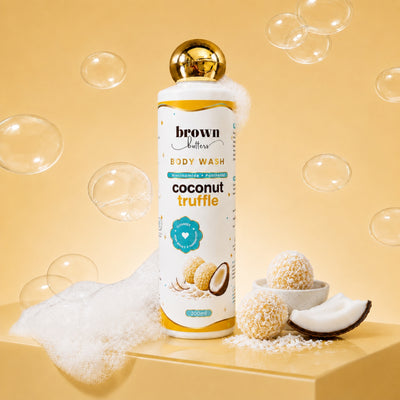 Brown Butters Coconut Truffle Body Wash bottle on a yellow pedestal with bubbles, foam and coconut props