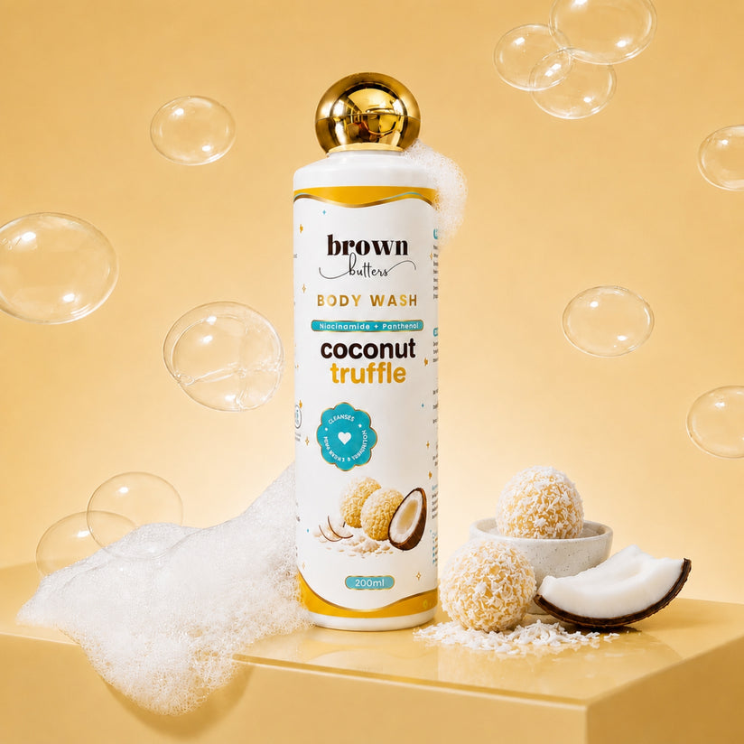 Brown Butters Coconut Truffle Body Wash bottle on a yellow pedestal with bubbles, foam and coconut props