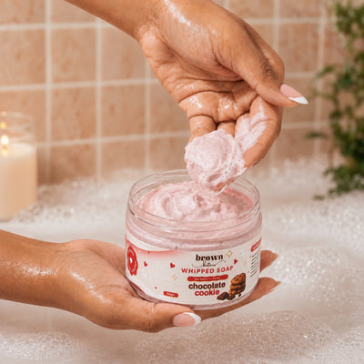 Brown Butters Chocolate Cookie Whipped Soap lifted from its jar by hand in a bubbly bathroom setting