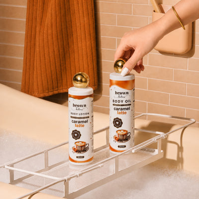 Brown Butters Caramel Latte lotion and oil on a white bath rack, a hand touching the oil bottle.