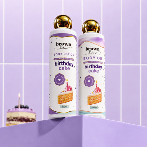 Brown Butters Birthday Cake Dessert Glow Duo lotion and oil on a purple pedestal, lavender tiled wall.